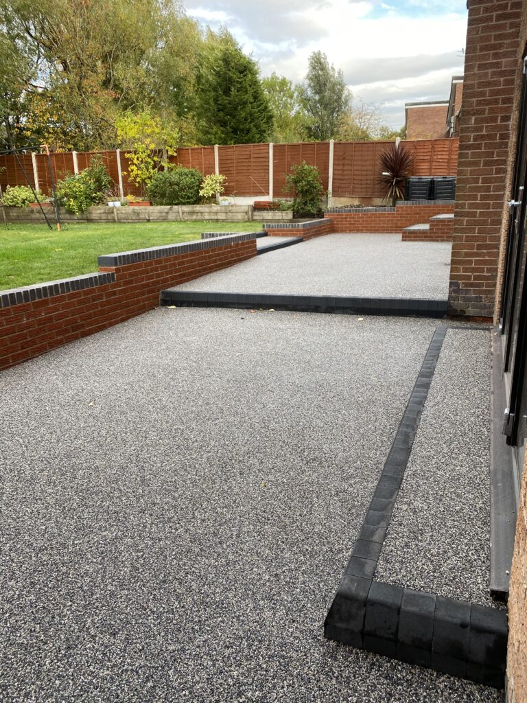 Grey resin patio with charcoal block borders and raised garden levels
