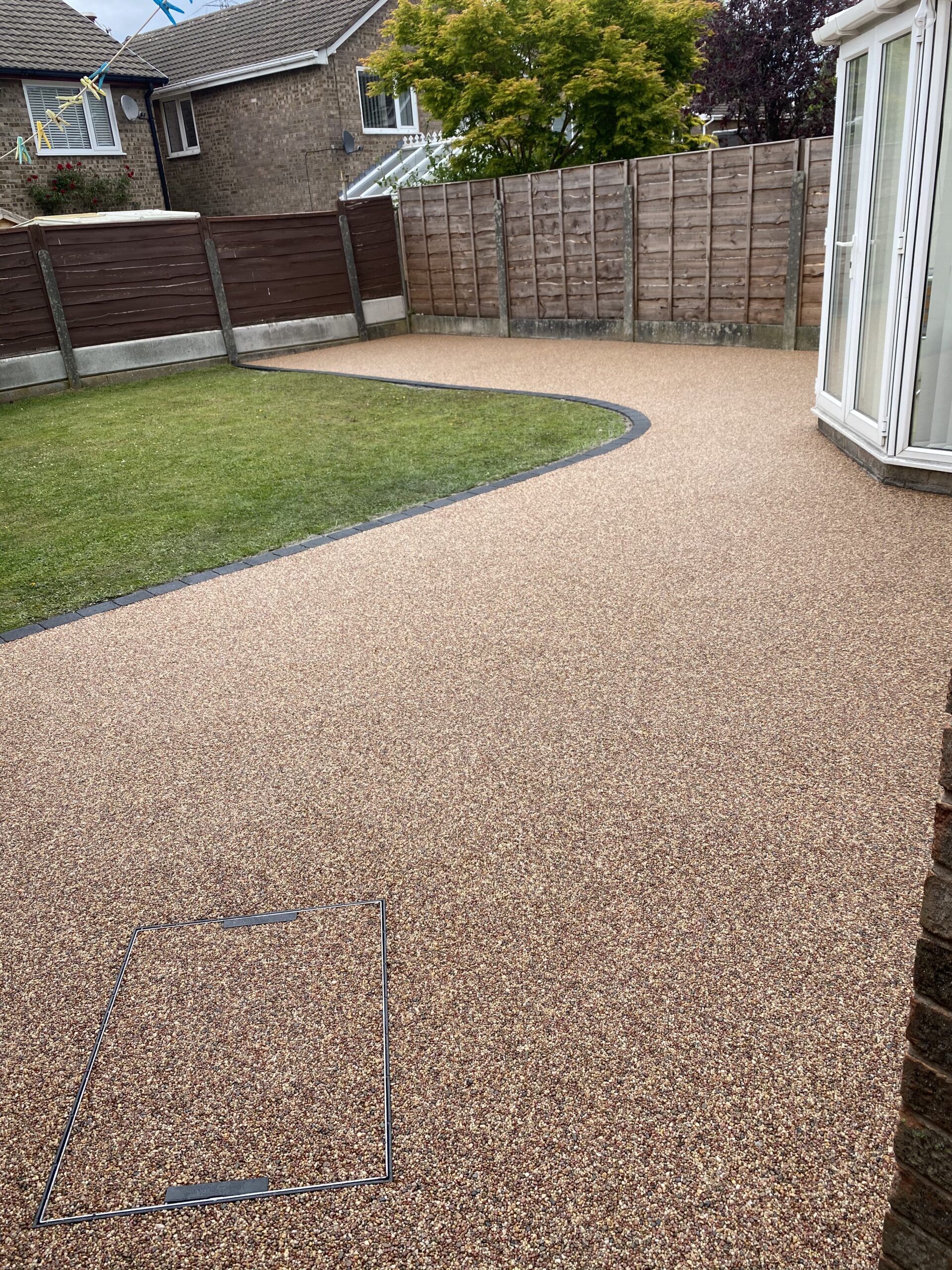 Sienna resin-bound patio in Offerton, Stockport with curved charcoal block edging around the lawn