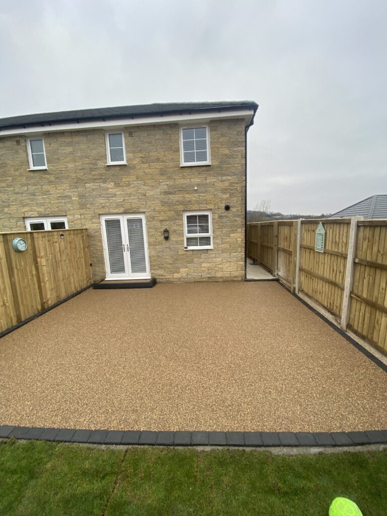 Natural stone resin patio with dark block border outside a modern home