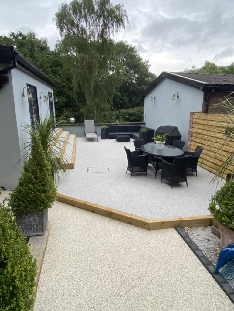 Light grey resin patio with raised timber edging and outdoor dining area